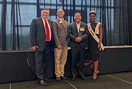  four people stand together with the one who is second from the right holding an award